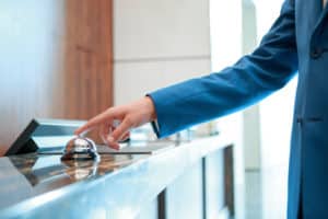 Service, please. Closeup of a businessman hand ringing silver service bell on hotel reception desk