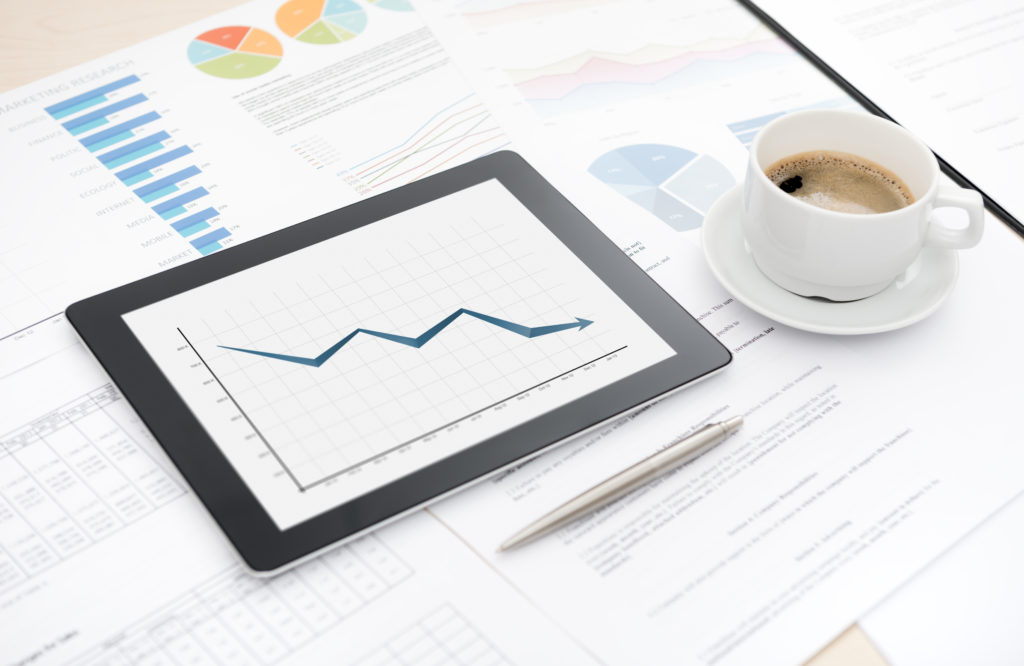 Desktop with bad statistic report on a modern digital tablet, some papers with charts and graphs and with a cup of coffee.